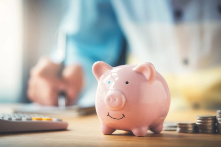 A piggy bank, coins and a calculator sitting before a man writing at a desk
