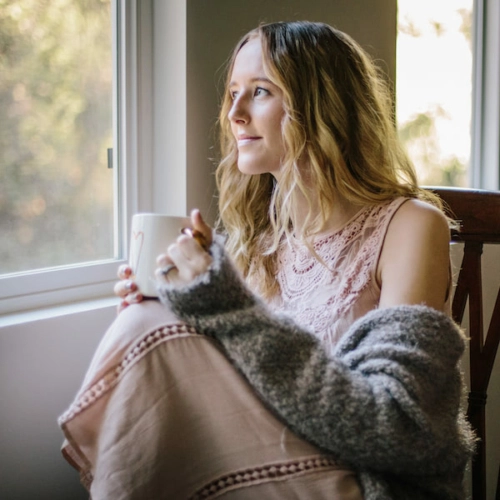 Woman with hot beverage in front of window