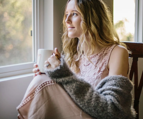 Woman with hot beverage in front of window