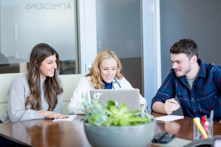 a doctor and 2 patients looking at a laptop sitting at a conference table