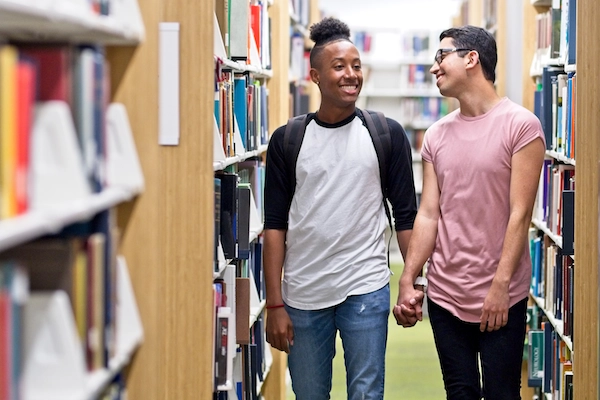 2 teens in library school holding hands and smiling