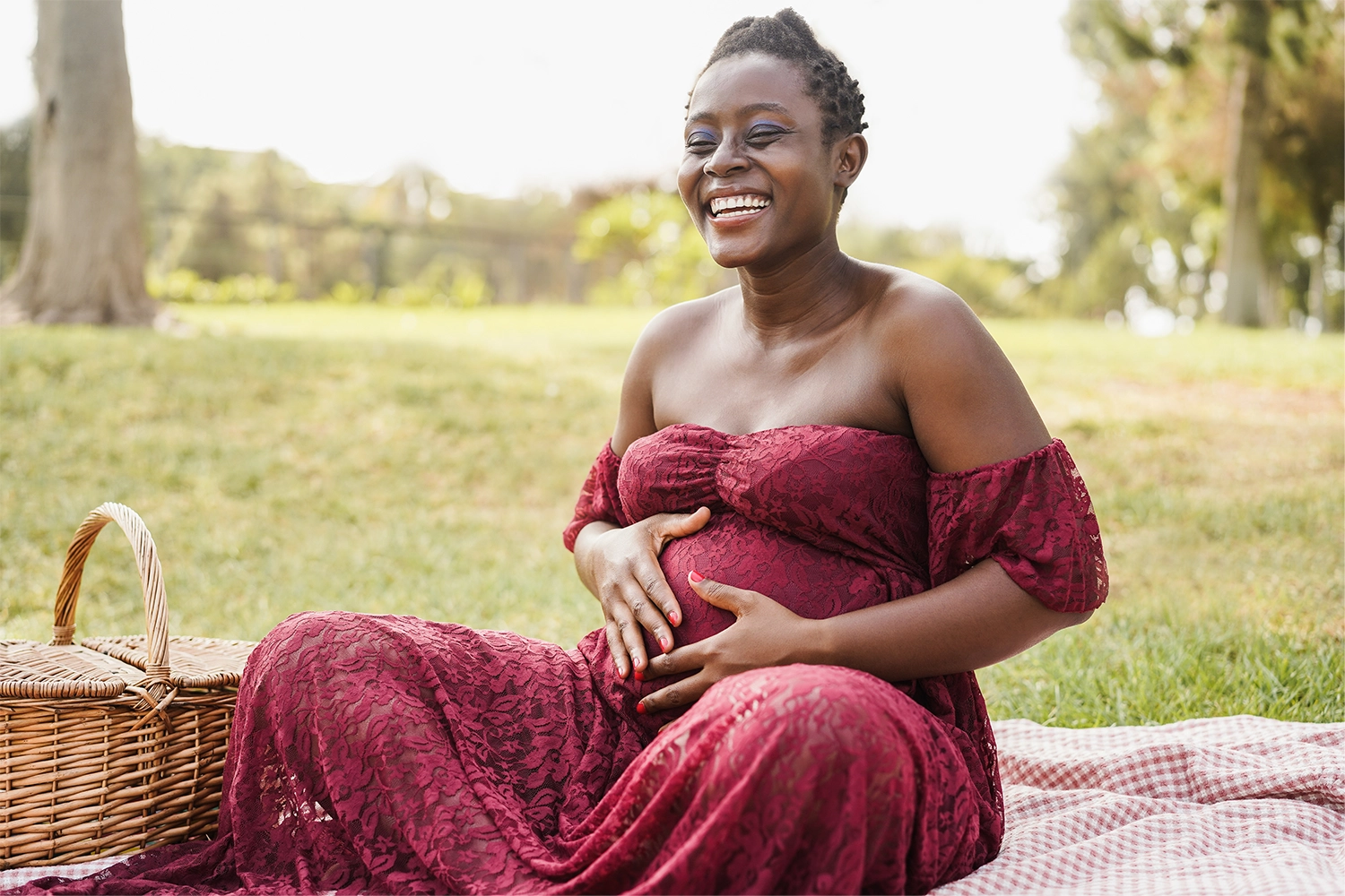 smiling pregnant woman sitting outside on blanket