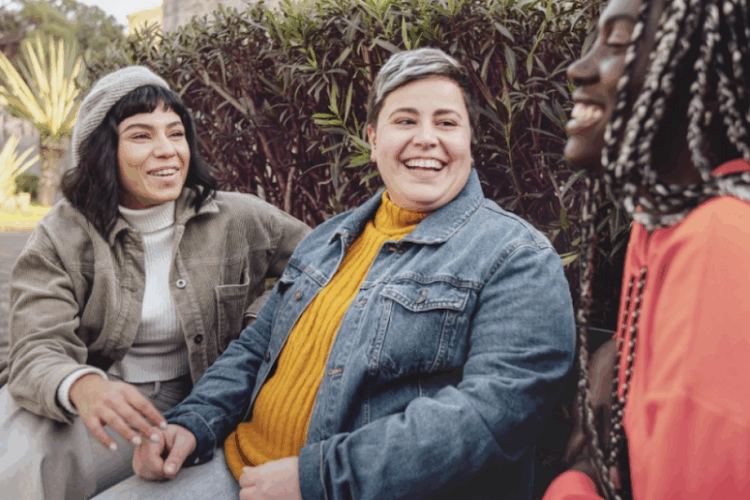 3 LGBTQ+ friends sitting and laughing on a bench.