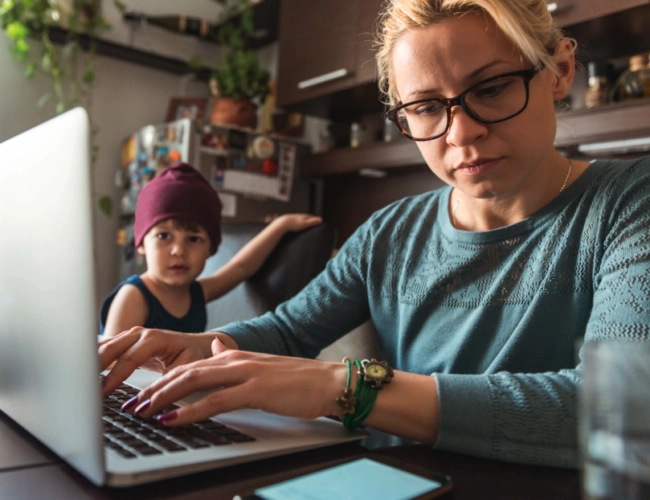 woman working on computer with small child next to her.