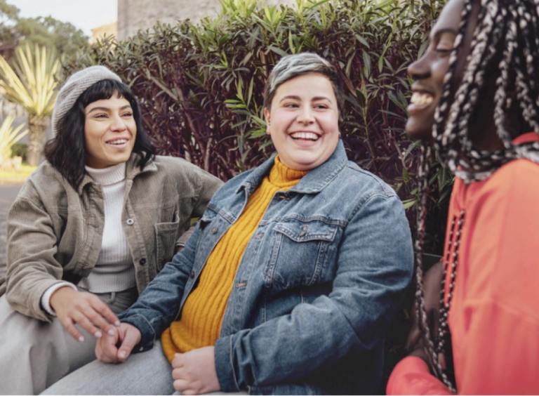 3 LGBTQ+ friends sitting and laughing on a bench.