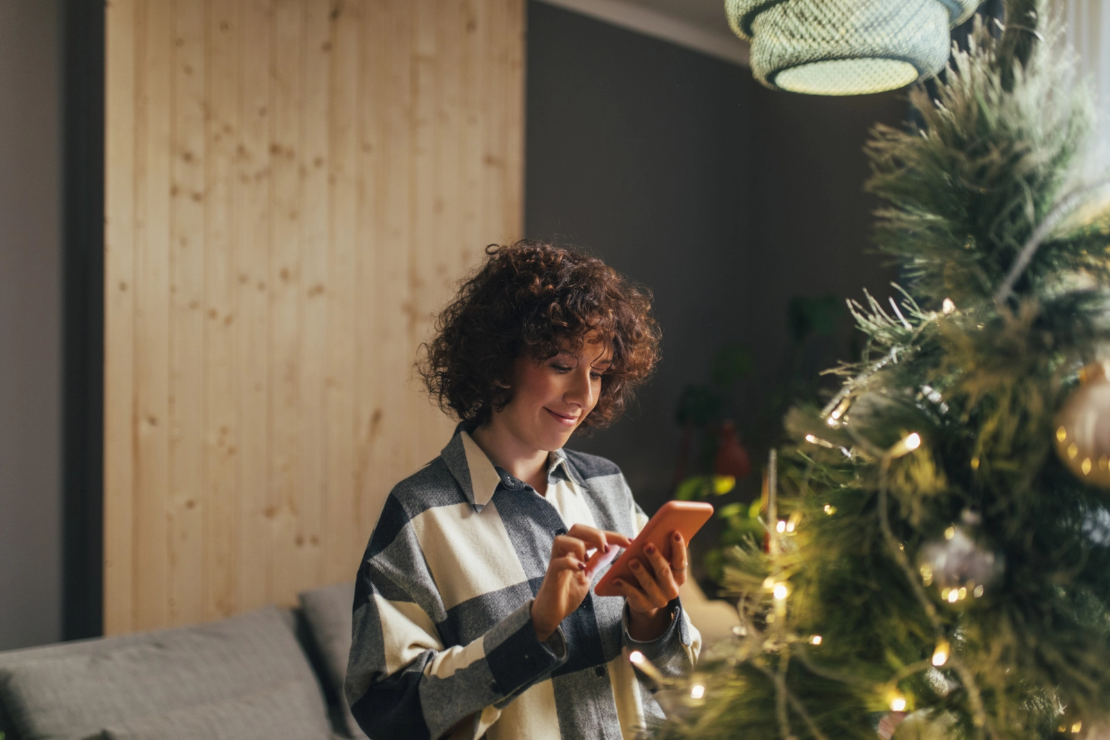 woman looking at phone near her Christmas tree