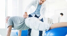 person stretching on exercise balls doing physical therapy with a therapist