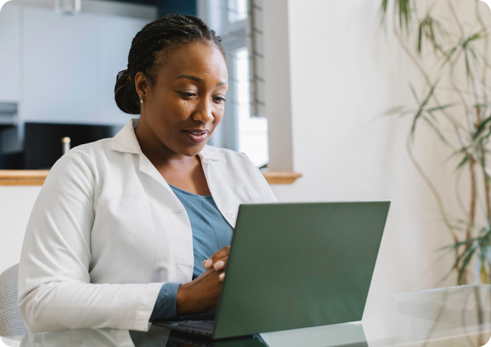 A smiling doctor in a white doctor coat looks at her computer