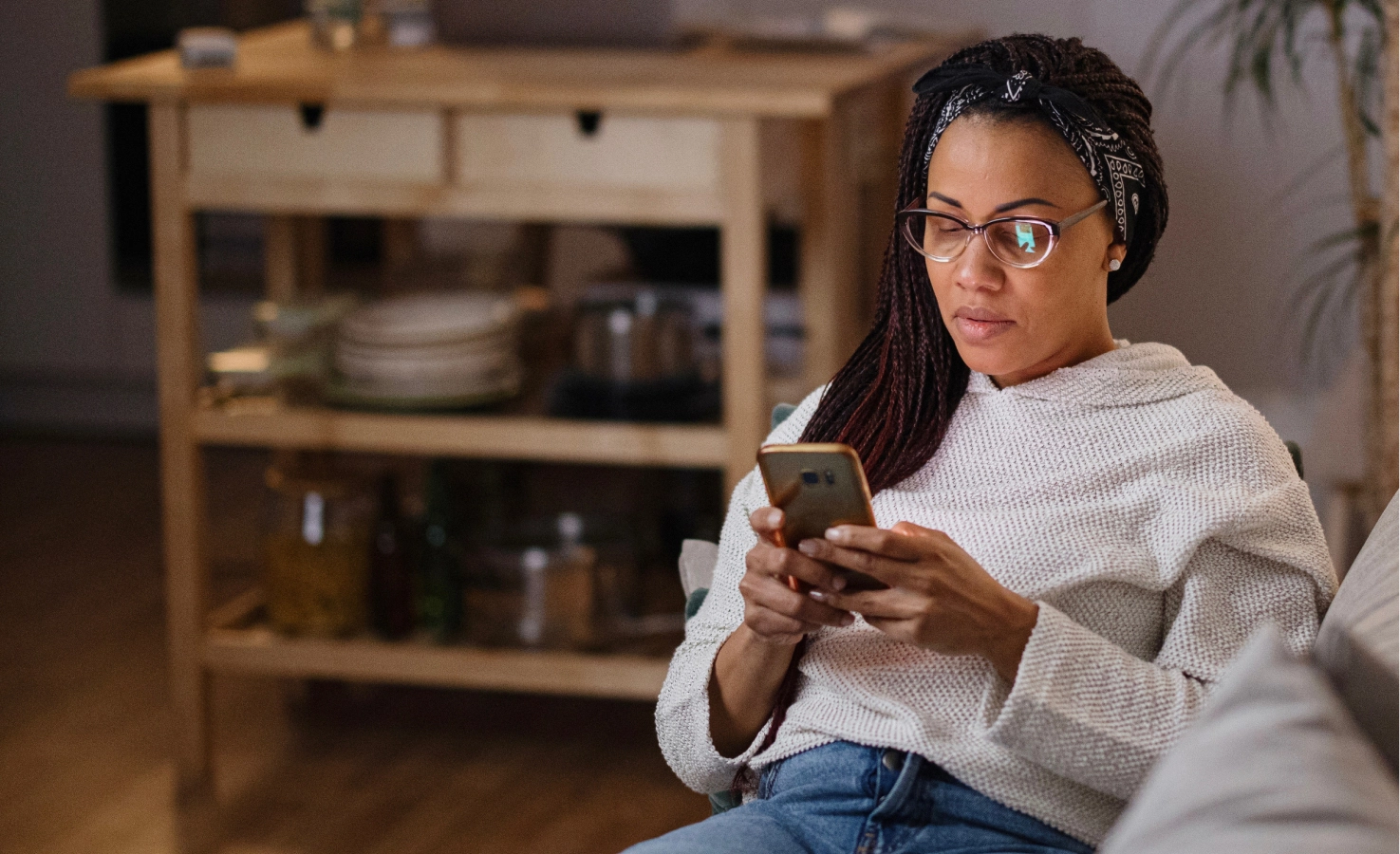 A woman sits on her couch and books an online psychiatry visit from her phone