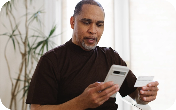 A black man holds his insurance card in one hand, his phone in the other