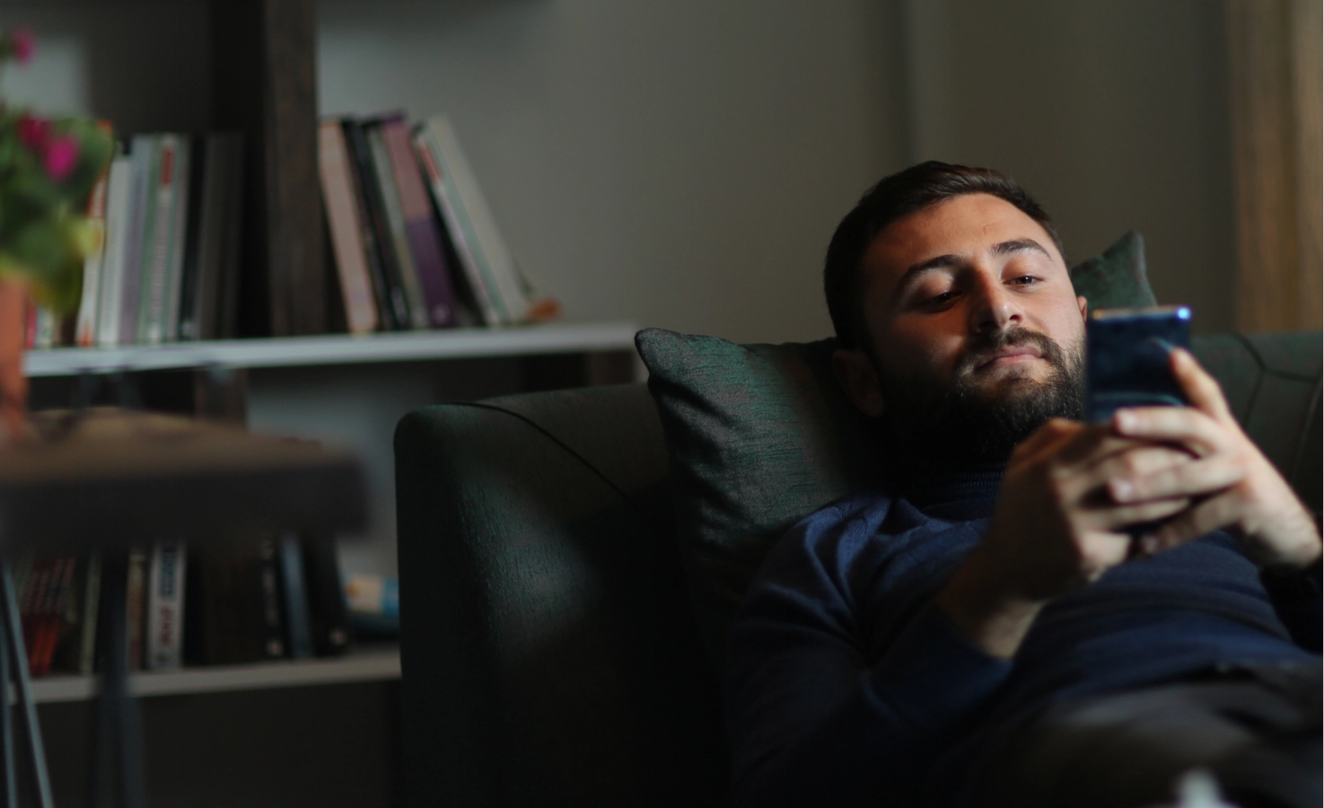 Photograph of a man laying on the sofa on his phone scheduling behavioral health.