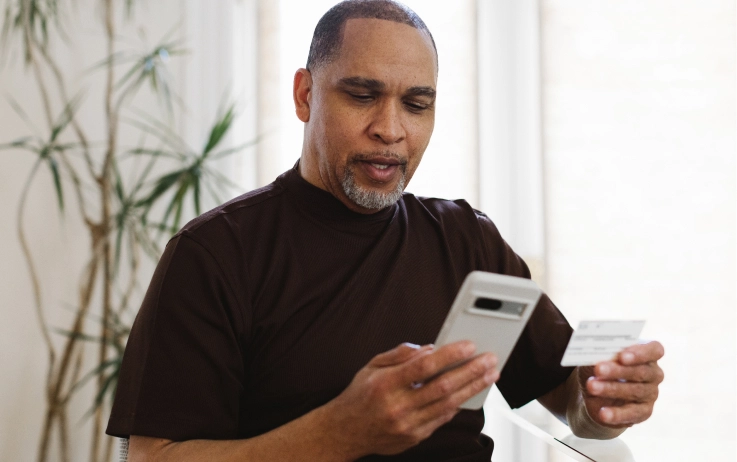 A man holds his insurance card in one hand, his phone in the other.