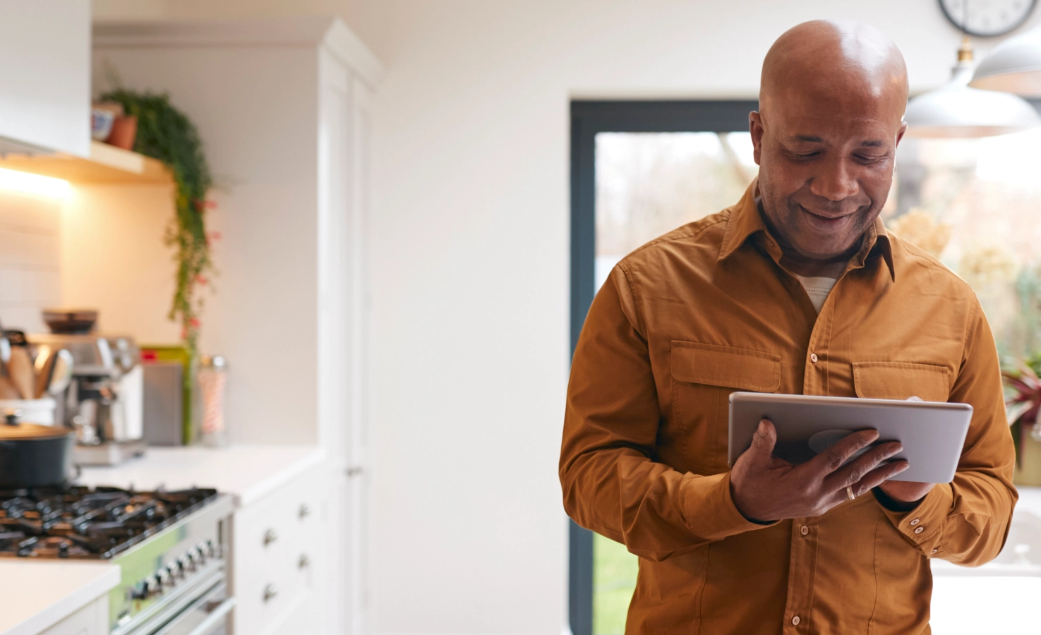 A man stands in his kitchen while browsing his health benefits from his tablet