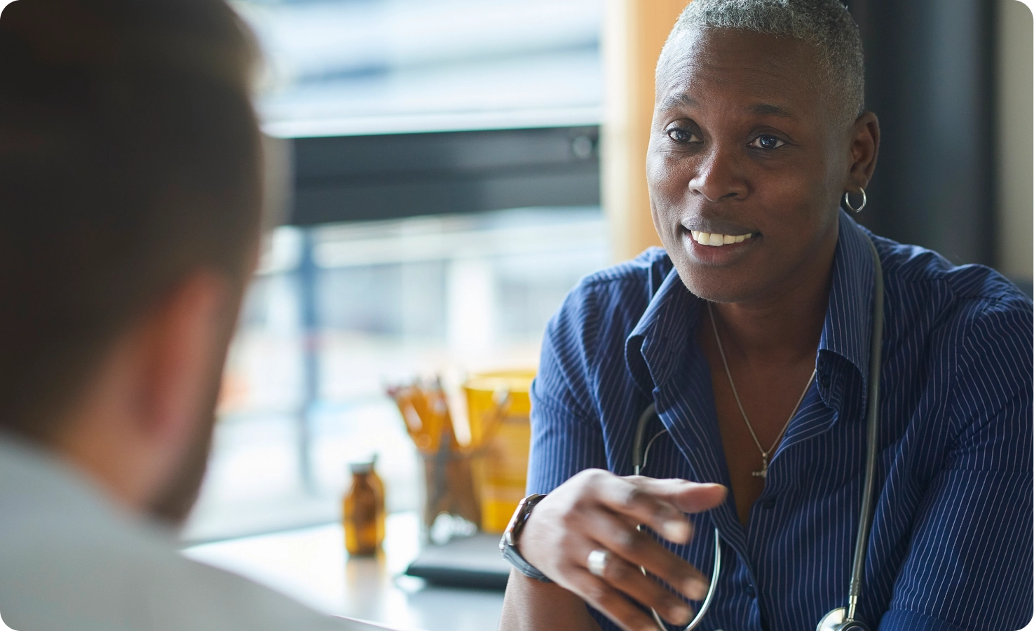 A Black doctor speaks with an LGBTQ+ patient in her office