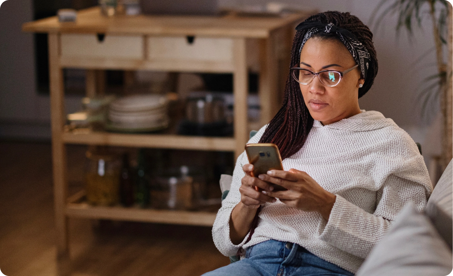 A woman sits on her couch and books an online psychiatry visit from her phone