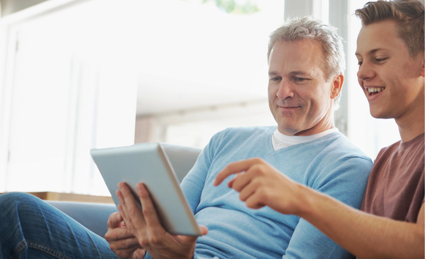 Two men sitting on couch looking at ipad.