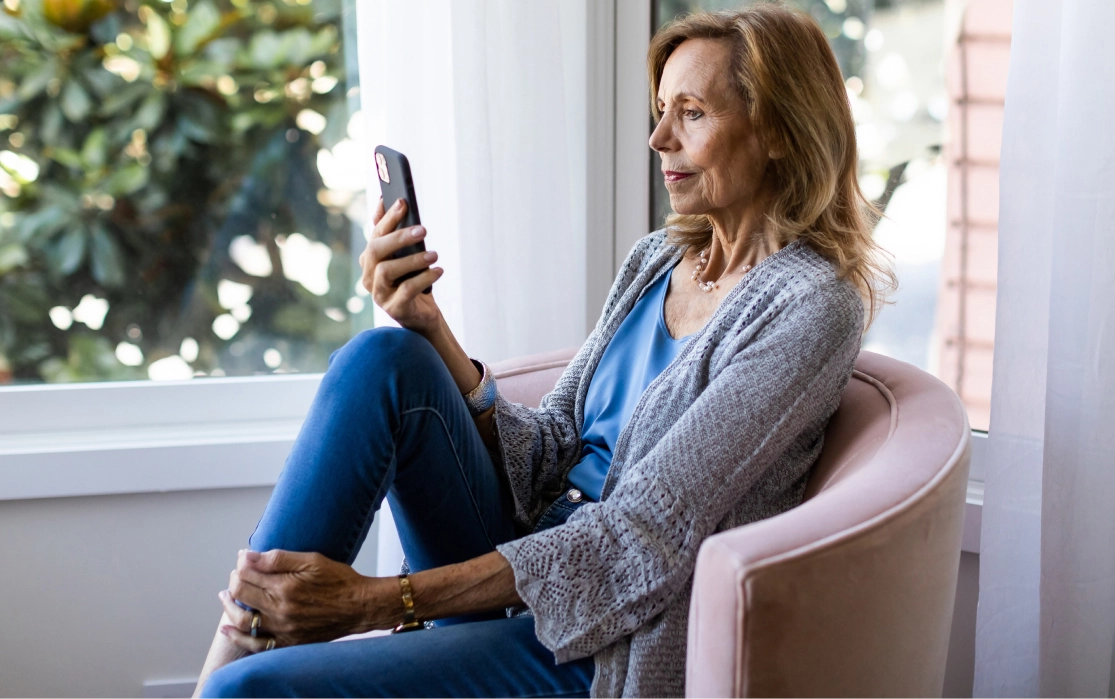 Woman sitting on chair looking at phone taking telehealth visit
