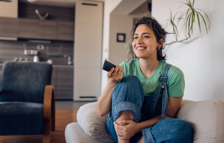 girl smiling on couch holding remote control