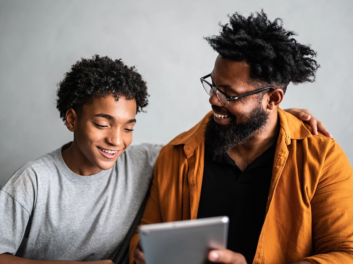 Father and son sitting together looking at computer and taking an online therapy session.