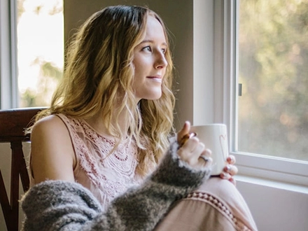 Woman holding cup of tea looking out of her window.