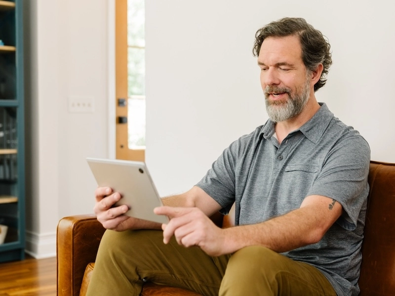 man sitting on couch using his tablet for a telehealth visit.