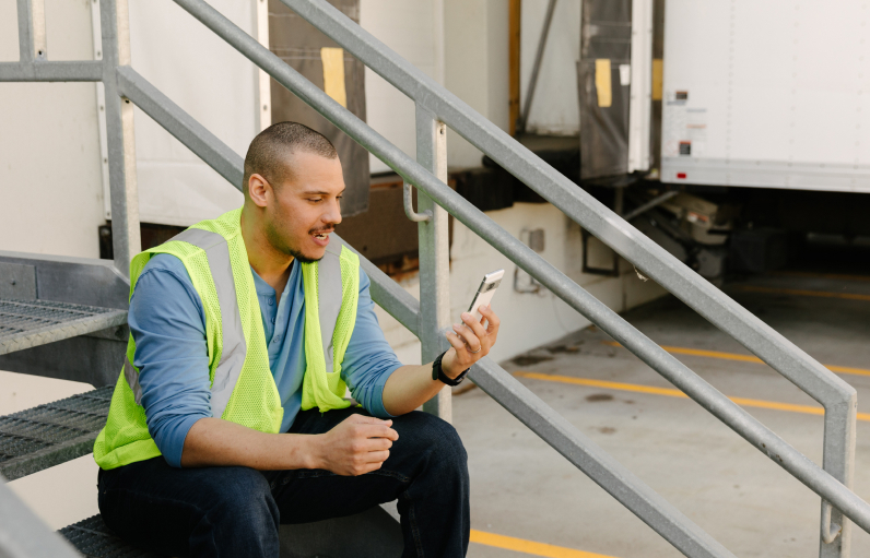 Worker with fluorescent vest on sitting outside on stairs taking a break and checking his phone.