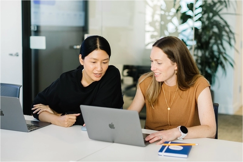 two female coworkers looking at laptop computer at desk.