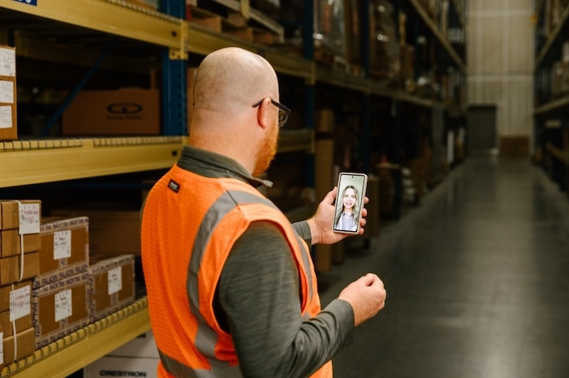 worker in a warehouse wearing an orange vest checking his mobile phone