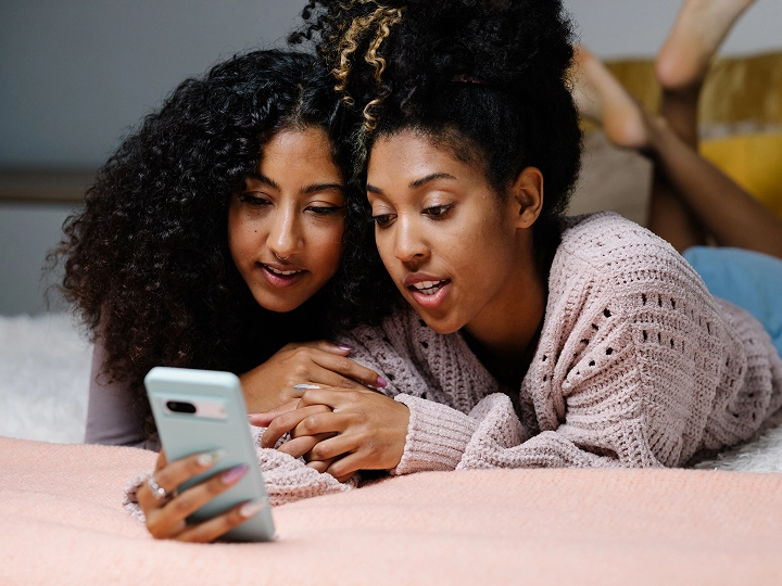 Two young adults looking at cell phone on bed.