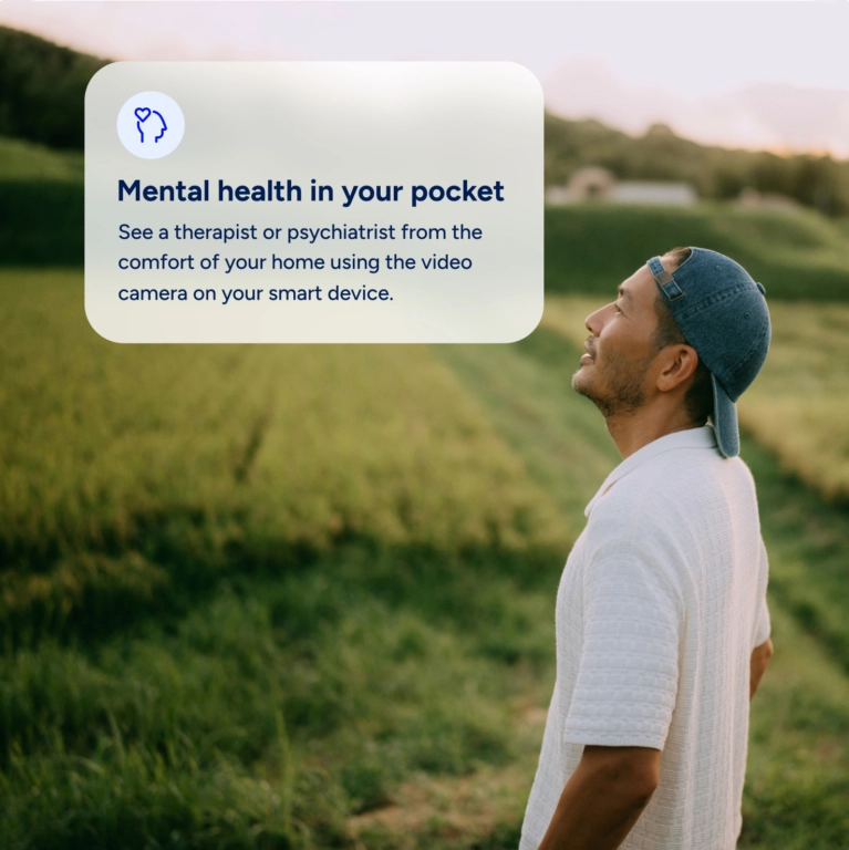 A man wearing a white shirt and a baseball cap stands in a grassy field, looking up at the sky. Overlaid on the image is a card that reads, "Mental health in your pocket. See a therapist or psychiatrist from the comfort of your home using the video camera on your smart device."
