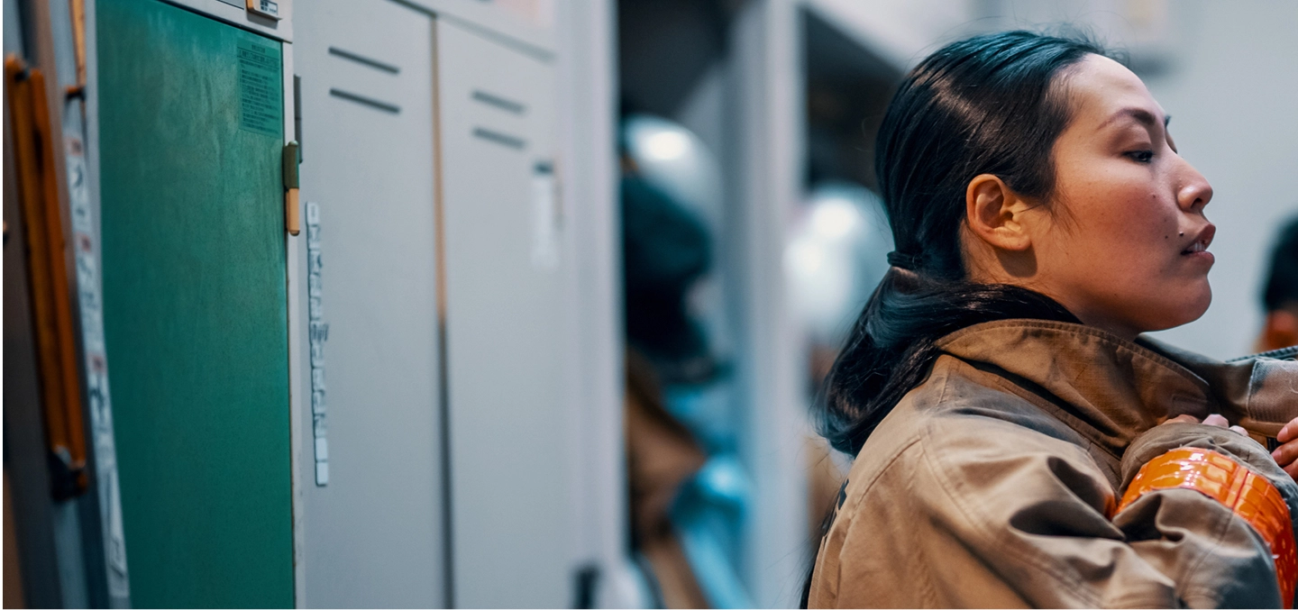 A close-up of a firefighter looking focused while putting on her protective gear in a locker room, highlighting dedication and readiness.