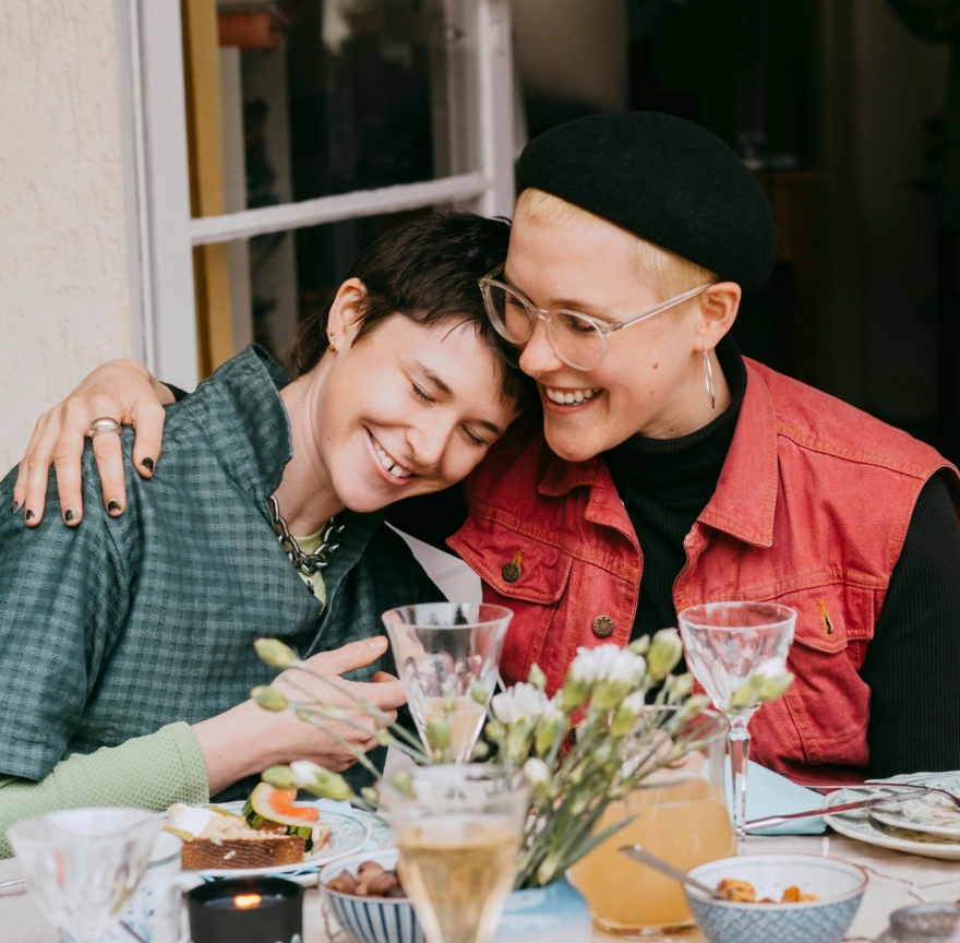 LGBTQ+ couple hugging at dinner table.