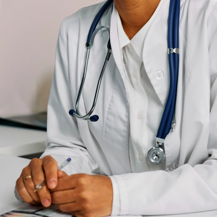 A close-up of a doctor in a white lab coat with a stethoscope. Overlaid on the image are two mobile app cards offering services: one to "Book therapy or psychiatry" (for all ages) and one to "Book primary care visit" (with availability noted as "