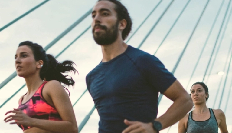 A diverse group of three runners in athletic wear exercising outdoors on a bridge. The image captures a sense of movement and fitness.