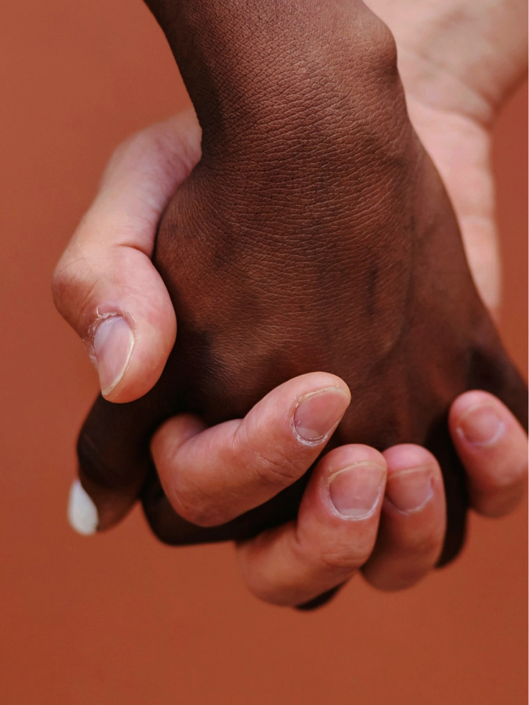 A close-up shot of two people of different races holding hands tightly, symbolizing support, trust, or solidarity in a healthcare context.