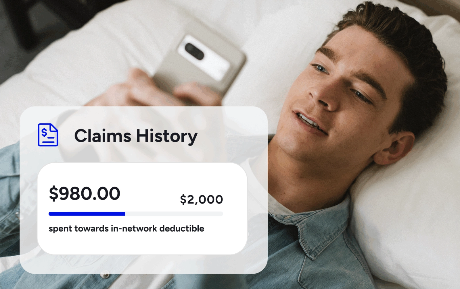 A young man lying in bed looks at his smartphone, which displays a health insurance "Claims History" screen showing $980.00 spent towards a $2,000 in-network deductible.