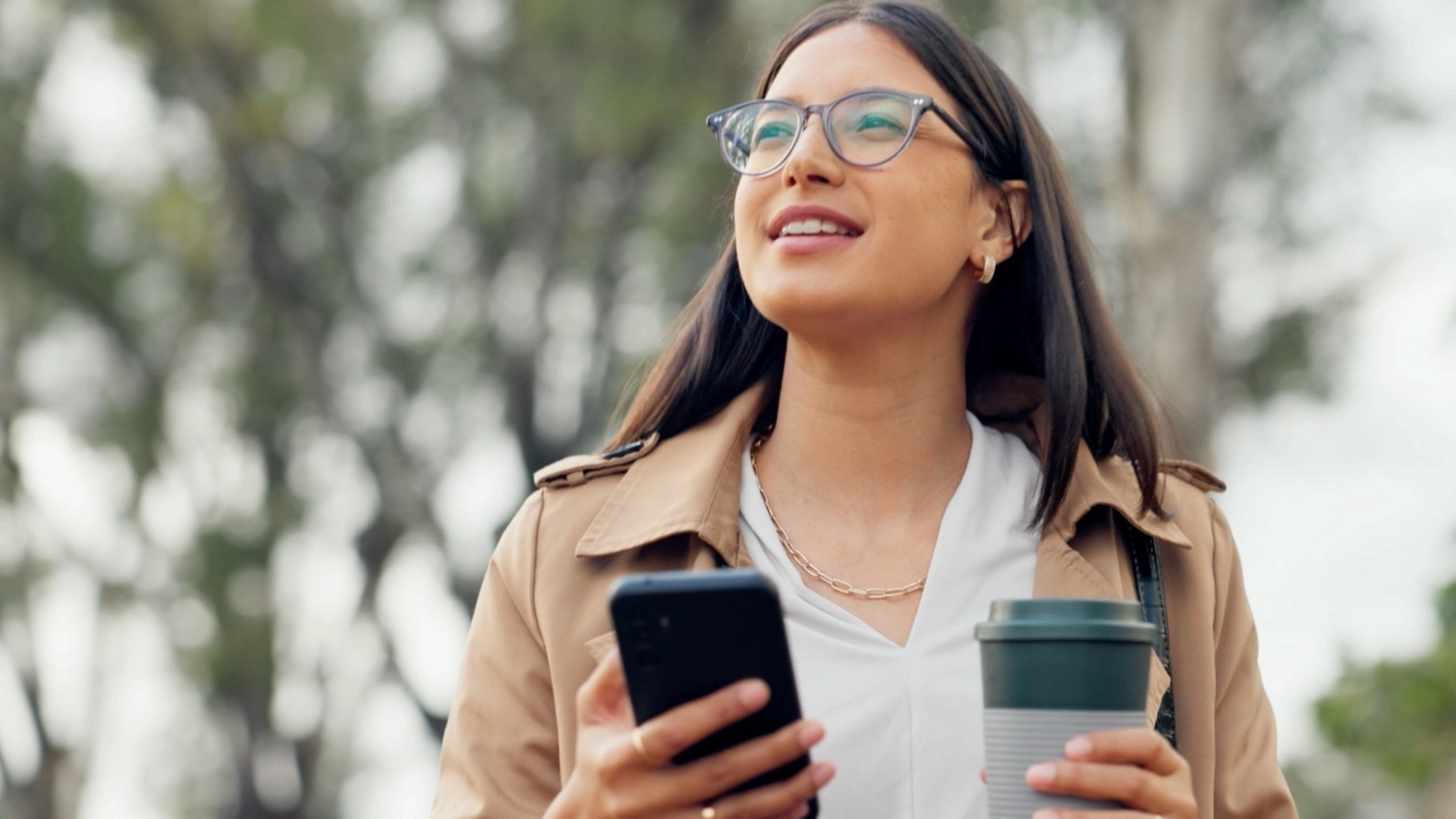 woman walking in park with phone and coffee