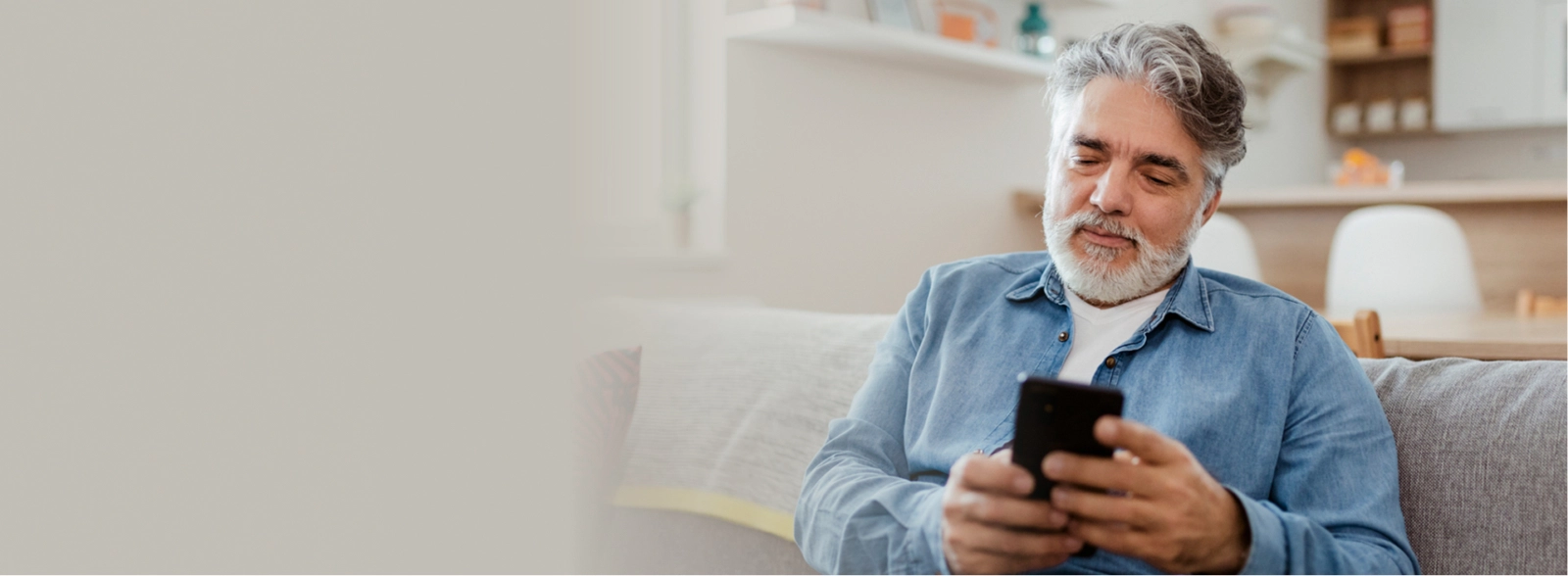 Older man sitting on a couch and using his phone