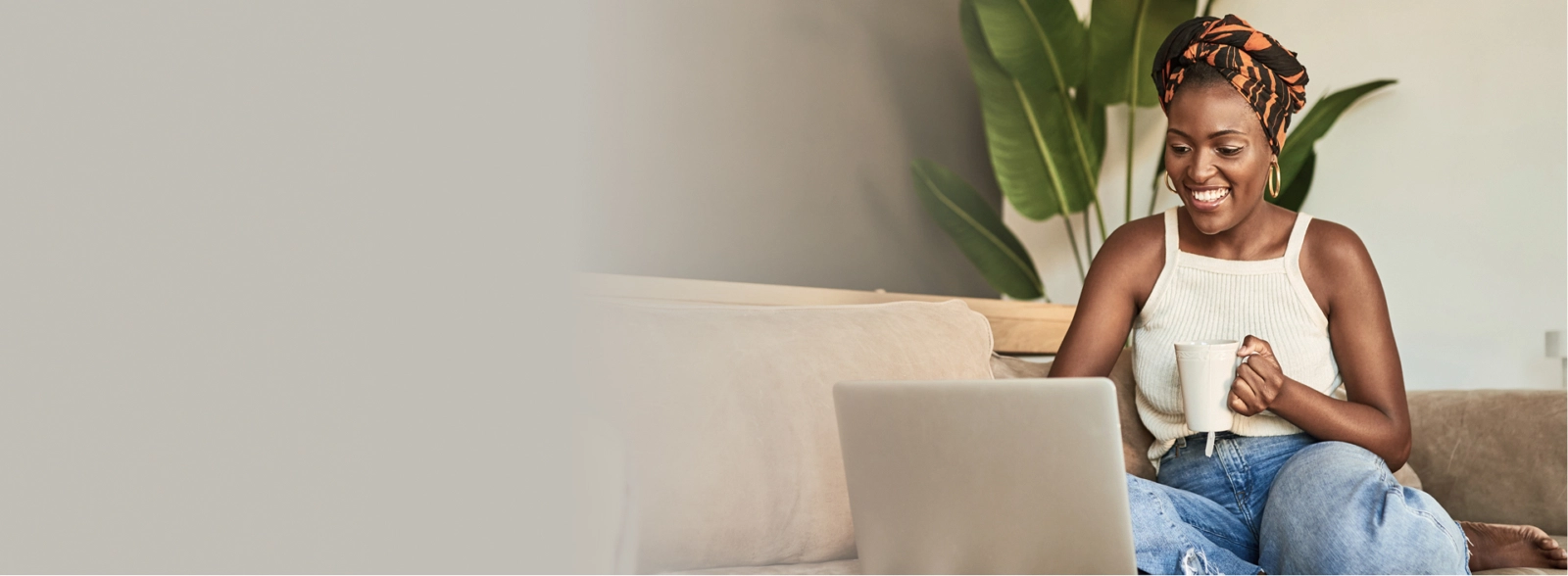 An African American woman sitting on a couch and using her laptop.