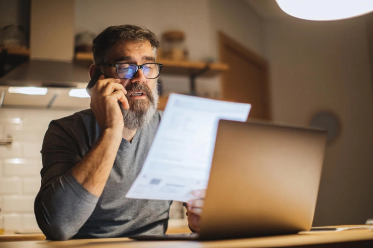A man reviewing a document while working on his computer.