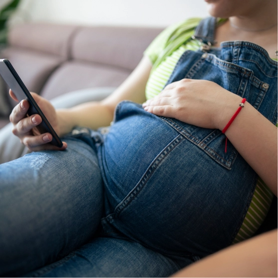 Close up of woman with pregnant belly in jeans looking at her phone. App interface overlays the image. It says: Hello Shannon. How can I help you this morning.